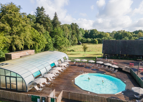 Piscina al aire libre con tumbonas y sombrillas en Huttopia Calvados - Normandie, rodeada de árboles y naturaleza.
