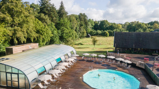 Piscina al aire libre con tumbonas y sombrillas en Huttopia Calvados - Normandie, rodeada de árboles y naturaleza.
