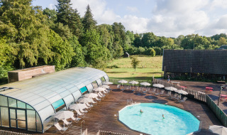 Piscina al aire libre con tumbonas y sombrillas en Huttopia Calvados - Normandie, rodeada de árboles y naturaleza.