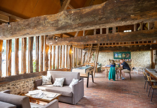 Intérieur convivial à Huttopia Calvados - Normandie, poutres en bois, canapés, jeux de société et ambiance chaleureuse.