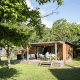 Wooden cabin with terrace surrounded by trees at Huttopia Calvados - Normandie holiday park in Normandy, France.
