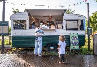 En kvinde med to børn bestiller mad ved en retro madvogn i ferieparken Huttopia Calvados, Normandiet.
