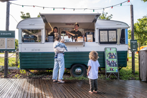 Una mujer con dos niños pide comida en un food truck vintage en el parque vacacional Huttopia Calvados, Normandía.