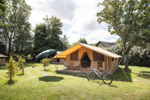 Una tienda espaciosa con terraza, bicicleta y sombrilla en Huttopia Calvados - Normandie, parque vacacional en Francia.