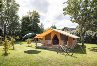 Et rummeligt telt med terrasse, cykel og parasol i Huttopia Calvados - Normandie feriepark, Frankrig.