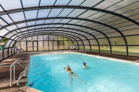 Piscina cubierta con dos personas nadando en el parque vacacional Huttopia Calvados - Normandie, en Normandía, Francia.