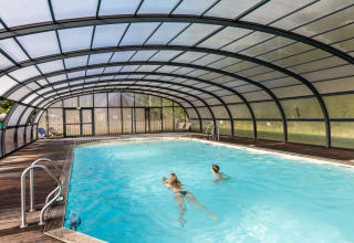 Overdækket swimmingpool med to personer, der svømmer, i ferieparken Huttopia Calvados - Normandie, Frankrig.