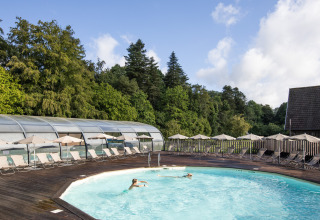 Udendørs poolområde med liggestole og parasoller i Huttopia Calvados - Normandie, feriepark i Frankrig.