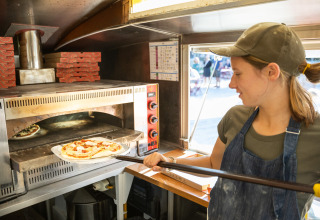 Kvinde bager frisk pizza i stenovn ved Huttopia Calvados - Normandie feriepark i Normandiet, Frankrig.
