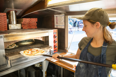 Mujer horneando pizza fresca en horno de piedra en Huttopia Calvados - Normandie, parque vacacional en Normandía, Francia.