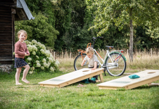 Zwei Kinder spielen draußen ein Wurfspiel neben einem Fahrrad im Huttopia Calvados, Normandie, Frankreich.