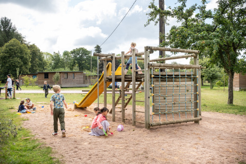Niños juegan en un parque infantil con tobogán y trepador en Huttopia Calvados - Normandie, parque vacacional en Francia.