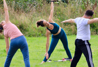 Gruppe mennesker udøver udendørs yoga på grønt græs i fredelig natur ved Huttopia Calvados - Normandie.