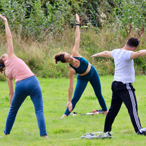 Personas practicando yoga al aire libre sobre césped verde en Huttopia Calvados - Normandie, Francia.