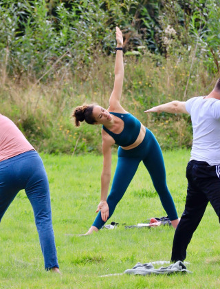 Personas practicando yoga al aire libre sobre césped verde en Huttopia Calvados - Normandie, Francia.