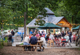Mennesker samles udendørs ved borde under lyskæder ved Huttopia Lac de Sillé, Pays de la Loire.