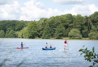 Folk dyrker vandsport som kajaksejlads og paddleboarding på en sø nær Sillé-le-Guillaume i Frankrig.