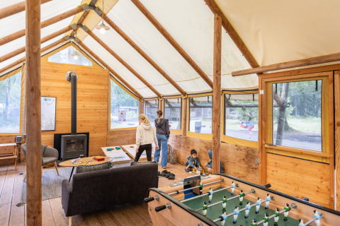 Cozy lodge interior at Huttopia Lac de Sillé, France, with families playing games and panoramic forest views.