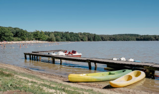 Orilla de lago cerca de Sillé-le-Guillaume, Pays de la Loire, Francia, con muelle, canoas y bañistas.