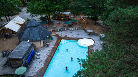 Vista aérea de una piscina y restaurante rodeados de árboles en Huttopia Lac de Sillé, Pays de la Loire, Francia.