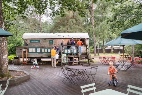 Kinder spielen im Außenbereich des Cafés von Huttopia Lac de Sillé im grünen Ferienpark in Frankreich.