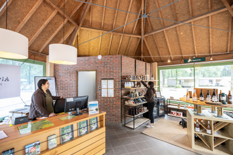 Recepción y tienda en Huttopia Lac de Sillé en Francia, con dos mujeres y productos locales en estantes.