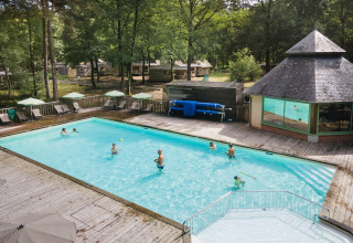 Swimmingpool med gæster omgivet af træer, solsenge og parasoller i ferieparken Huttopia Lac de Sillé, Frankrig.