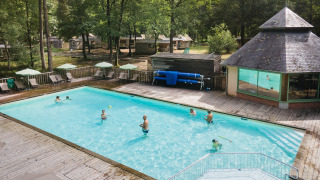 Personas nadando y relajándose en la piscina al aire libre de Huttopia Lac de Sillé rodeada de naturaleza, Francia.