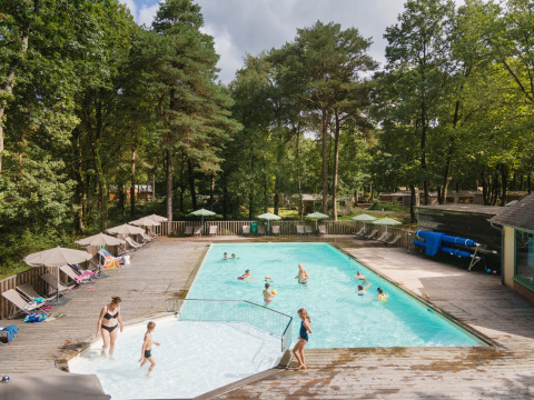 Buitenzwembad omringd door bos, gezinnen ontspannen en zwemmen bij Huttopia Lac de Sillé vakantiepark.