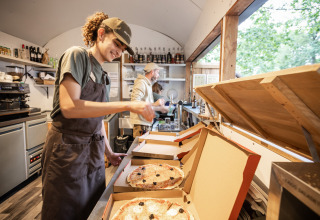 Dos empleados meten pizzas recién hechas en cajas dentro de la cocina de Huttopia Lac de Sillé, Francia.