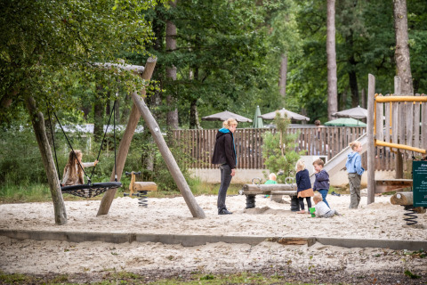 Kinderen spelen en een volwassene houdt toezicht op een zand-speelplaats bij Huttopia Lac de Sillé, Frankrijk.