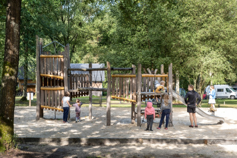 Kinderen spelen op een houten speeltoestel tussen de bomen bij Huttopia Lac de Sillé in Frankrijk.