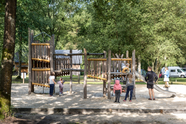 Children and adults enjoy a wooden playground surrounded by trees at Huttopia Lac de Sillé, France.