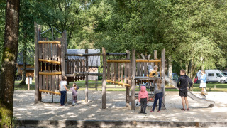 Niños y adultos juegan en un parque infantil de madera rodeado de naturaleza en Huttopia Lac de Sillé, Francia.