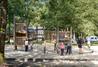 Niños y adultos juegan en un parque infantil de madera rodeado de naturaleza en Huttopia Lac de Sillé, Francia.