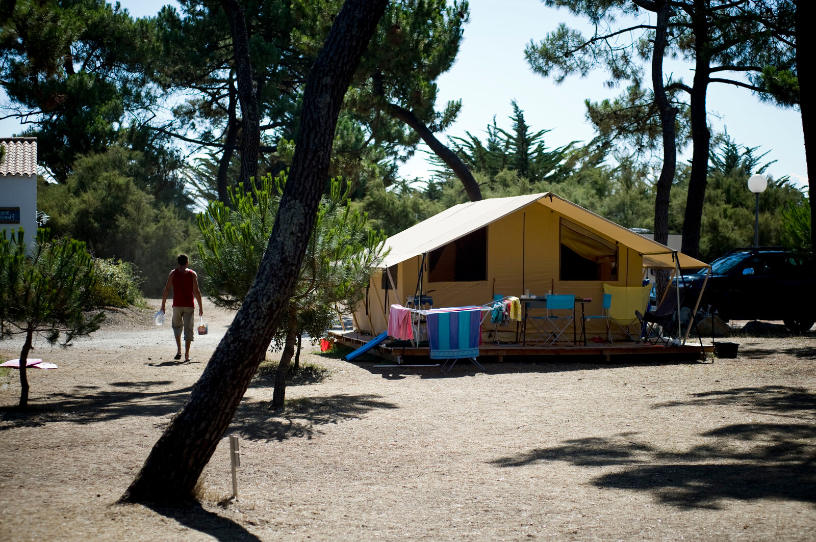 Klassieke Toile&bois safaritent op een zonnige camping met stoelen, tafels en kleurrijke handdoeken.