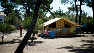 En klassisk Toile&bois safariteltsplads med stole, borde og farverige håndklæder på en solrig campingplads.