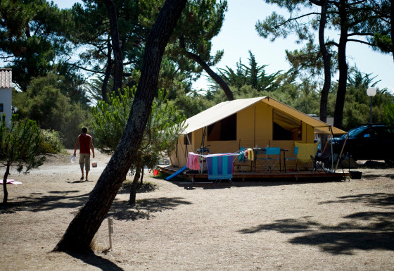 Tenda safari Toile&bois classic in un campeggio soleggiato, con sedie, tavolo e asciugamani colorati stesi.