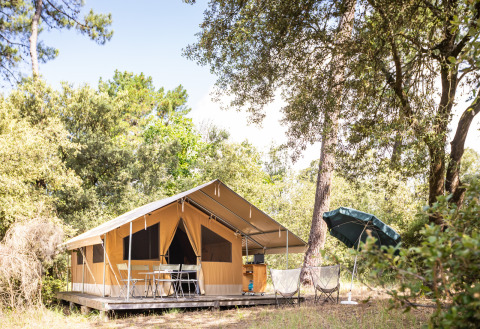 Safari teltet Toile&Bois Classic ved Huttopia Noirmoutier i Frankrig, omgivet af træer og udendørs møbler.
