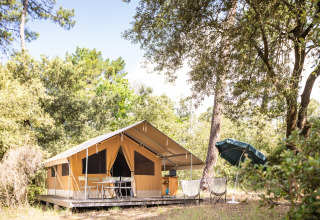 Safari teltet Toile&Bois Classic ved Huttopia Noirmoutier i Frankrig, omgivet af træer og udendørs møbler.