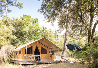 Tenda safari Toile&bois Classic all'Huttopia Noirmoutier in Francia, immersa tra alberi e arredi da esterno.
