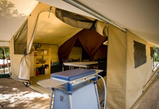 Foto interior de una tienda safari Toile&bois Classic en Huttopia Noirmoutier, Francia, con suelo de madera y muebles de camping.
