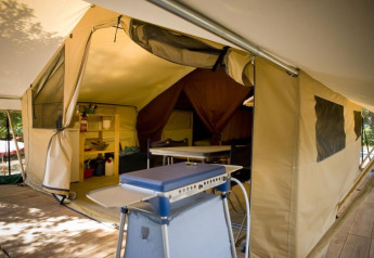 Foto interior de una tienda safari Toile&bois Classic en Huttopia Noirmoutier, Francia, con suelo de madera y muebles de camping.