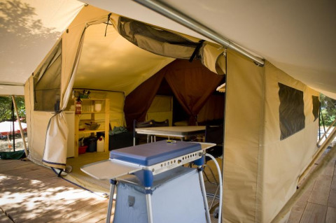 Foto interior de una tienda safari Toile&bois Classic en Huttopia Noirmoutier, Francia, con suelo de madera y muebles de camping.