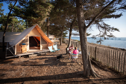 Tienda safari en la costa de Huttopia Noirmoutier, Francia, con dos personas disfrutando al aire libre.