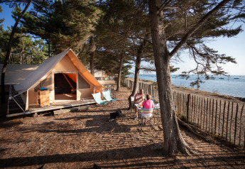 Tienda safari en la costa de Huttopia Noirmoutier, Francia, con dos personas disfrutando al aire libre.