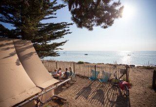 Famille dînant devant une tente Toile&Bois sur la côte à Huttopia Noirmoutier, France, avec vue sur mer.