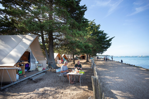 Folk sidder ved et bord foran safaritelte ved kysten på Huttopia Noirmoutier campingplads i Frankrig.