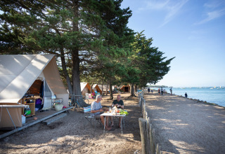Mensen aan een tafel voor safaritenten bij de kust op Huttopia Noirmoutier camping in Frankrijk.