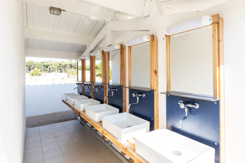 Bright, modern outdoor wash area with multiple sinks and mirrors at a glamping accommodation site.